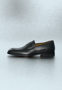 Μαύρο ανδρικό μοκασίνι από δέρμα με κομψό σχεδιασμό και λουράκι στο επάνω μέρος με ανάγλυφο το όνομα της μάρκας "Bally."