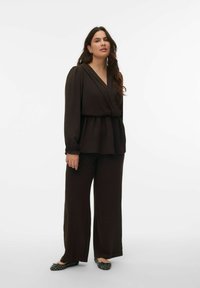 Blouse cache-cœur marron avec détails plissés, associée à un pantalon large assorti. La tenue présente des manches longues et un tissu doux à texture.