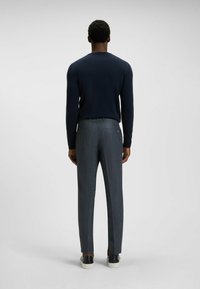 Navy knit sweater combined with textured gray trousers. Features tailored fit, back pocket accents, and contrasting footwear.