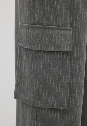 Pantalones a rayas grises con un gran bolsillo de cargo en el lateral, confeccionados en una suave tela texturizada y con un sutil detalle amarillo en las rayas.