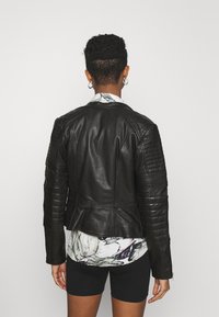 Svart lädermotorcykeljacka med ribbade axlar och ärmar, skräddarsydd passform och en slät yta. Buren över en blommig skjorta.