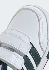 Sneaker sintetico bianco con due strap in velcro, strisce verdi e una finitura testurizzata. Punta arrotondata e dettaglio di cucitura a contrasto.