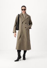 Cappotto doppiopetto in puro tessuto houndstooth marrone e crema, con una vestibilità ampia e un ampio colletto. Abbinato a stivali neri con tacco al ginocchio e una borsa nera.