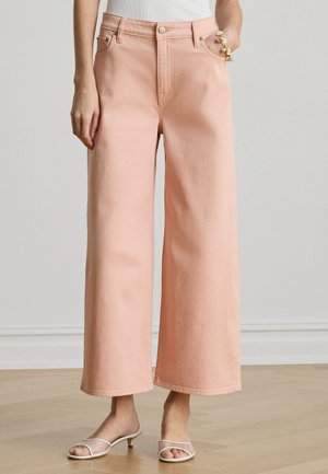 Lyserøde denimbukser med vide ben, båret med hvide sandaler med stropper og kitten-hæl samt et skaldyr-armbånd på den ene hånd.