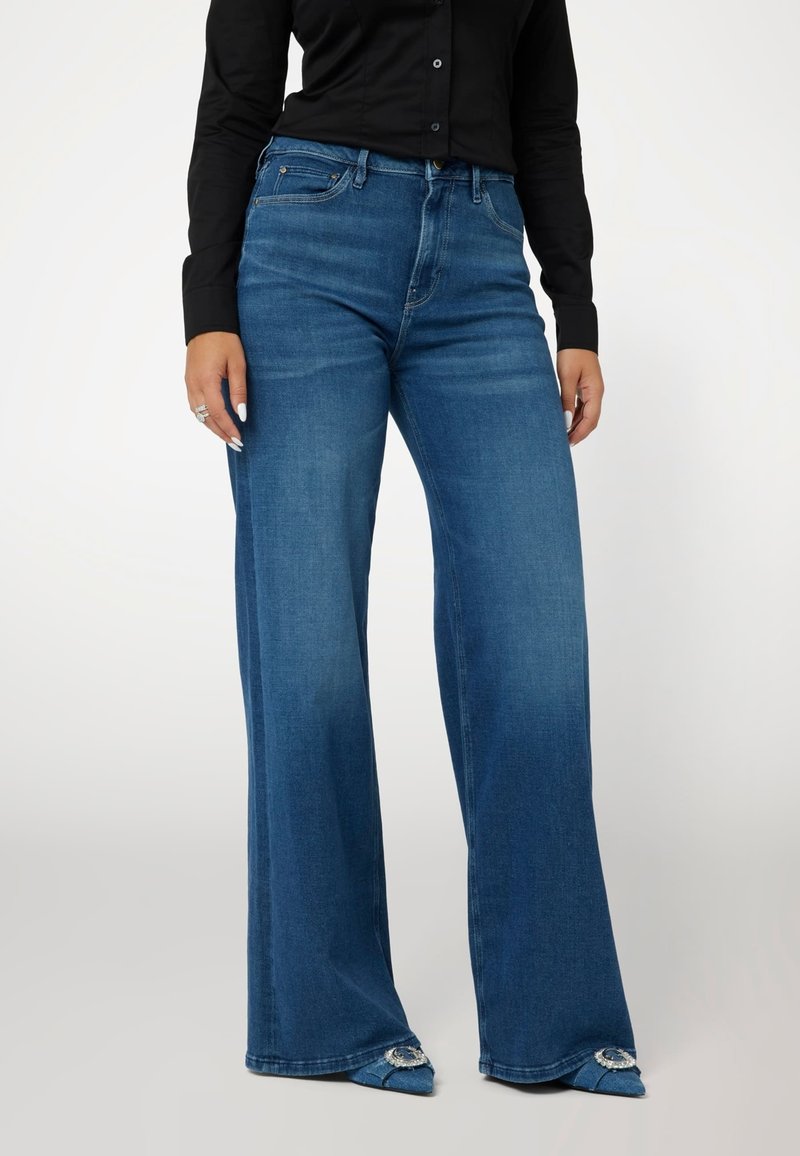 Plačios blauzdos mėlyni džinsai su išblukusiu plačiu, penkių kišenių dizainu ir mygtuko uždarymu. Sausas siluetas su tekstūruotu audiniu.