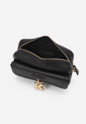 Sac rectangulaire en cuir noir avec fermeture éclair dorée partiellement ouverte et breloque dorée en forme de K accrochée à la tirette de la poche avant.