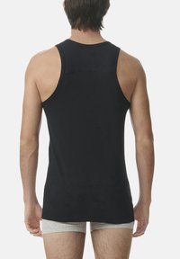 Top sin mangas negro con cuello redondo, textura suave y un diseño ajustado. El modelo lleva pantalones cortos grises debajo.