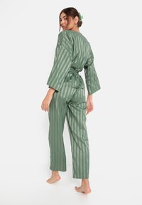 Groene gestreepte loungewear set met een losvallende kimono-mouwtop en bijpassende broek, gemaakt van een gladde stof met een strikdetail in de taille.
