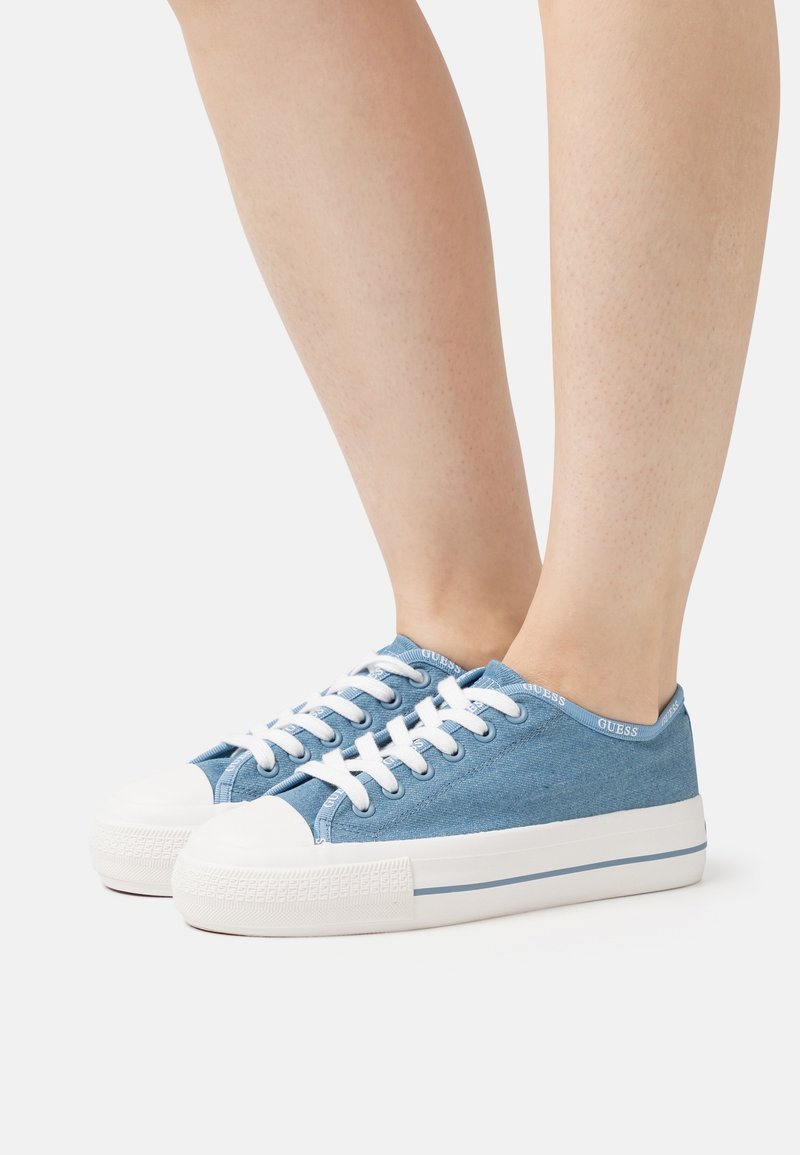 Niebieskie płócienne sneakersy z białą gumową osłoną palców i podeszwą, z białymi sznurowadłami i niebieskim akcentem marki na kołnierzu.