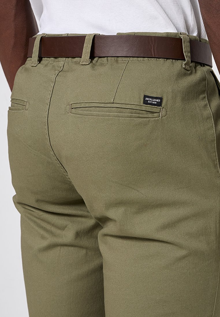 Olivgröna byxor i bomull med vävd textur, två bakfickor och ett brunt läderbälte med spänne.