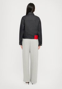 Mørk denimjakke med en cropped design, gul syning og et rødt mærke på ryggen. Sat sammen med grå vide benbukser.
