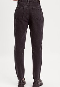 Jeans neri a vita alta con una vestibilità dritta, realizzati in denim. Presentano due tasche posteriori e dettagli di cucitura sottili.