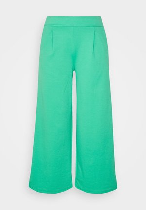 Felgroene broek met wijde pijpen, een elastische tailleband en plooien aan de voorkant, afgebeeld tegen een eenvoudige lichte achtergrond.