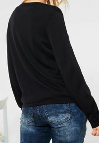 Suéter negro de manga larga con escote redondeado, combinado con jeans de mezclilla azul con un lavado desgastado y suturas sutiles en los bolsillos traseros.