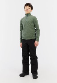 Pullover in pile verde con colletto a zip, abbinato a pantaloni neri larghi. Stivali neri completano l'outfit. Design semplice e funzionale.