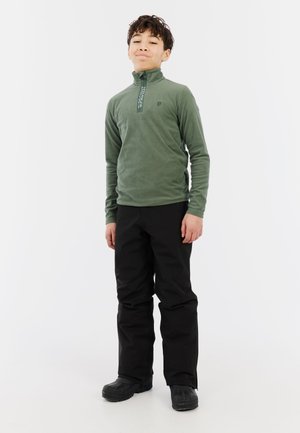 Groene fleece pullover met een ritskraag, gecombineerd met zwarte, losse broek. Zwarte laarzen maken het geheel af. Eenvoudig, functioneel ontwerp.