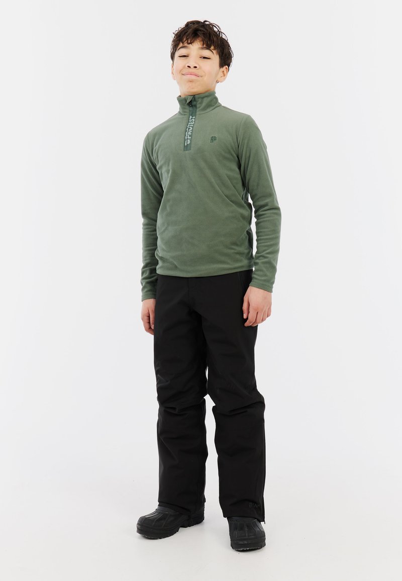 Pullover in pile verde con colletto a zip, abbinato a pantaloni neri larghi. Stivali neri completano l'outfit. Design semplice e funzionale.