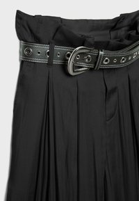 Jupe plissée noire taille haute avec une large ceinture en cuir noir équipée d'œillets argentés et d'une grande boucle argentée.