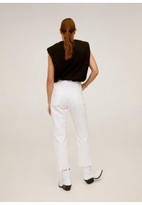 Top nero senza maniche con spalle strutturate, abbinato a jeans bianchi a vita alta a gamba dritta e stivali bianchi alla caviglia con tacchi neri.