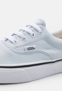 Světlomodré plátěné tenisky s bílými tkaničkami, černým prošíváním a gumovou podrážkou. Na boku se nachází malé logo Vans.