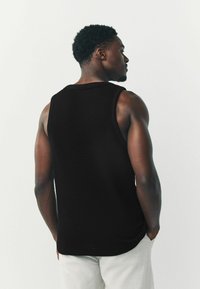 Zwarte mouwloze gebreide tanktop met een gemêleerd patroon, ronde hals en een relaxte pasvorm, gecombineerd met lichtgekleurde broeken.