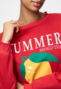 Sudadera roja con cuello redondo, que presenta un gráfico de un mango amarillo y el texto "ÁRBOL DE MANGO DE VERANO" en blanco. Tejido suave, detalles de costura visibles.
