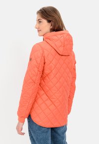 Gequilted oranje jack met een capuchon, voorzien van elastische manchetten en een logopatch op de schouder. Glad, lichtgewicht materiaal en afgeronde zoom.