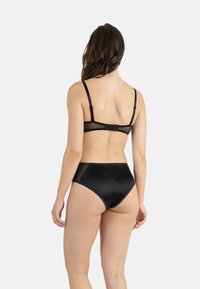 Ensemble de lingerie noire comprenant un soutien-gorge à dos en mesh transparent et une culotte haute. Texture lisse avec une coupe classique et un minimum de matériel.