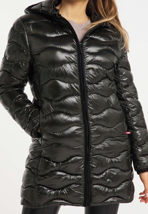 Femme portant une doudoune matelassée noire brillante avec une fermeture éclair à l'avant, une capuche et des poches latérales, debout devant un fond blanc.