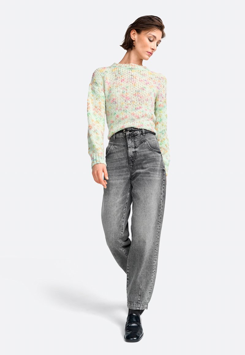Pull en tricot multicolore pastel à manches longues, associé à un jean en denim gris taille haute. Des chaussures noires complètent la tenue.