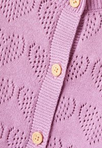 Lys rosa strikket cardigan med et teksturert hjerte-mønster, med treknapper og ribbede kanter. Mykt, koselig materiale.