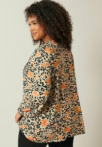 Løs pasform, langærmet top med en beige baggrund, sorte leopardpletter og orange blomsterdetaljer. Blødt stof, afslappet silhuet.