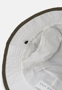 Chapéu bucket com exterior em algodão verde-azeitona e forro acolchoado branco. Apresenta uma aba circular e um acabamento costurado e durável.