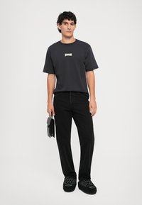 Camiseta de algodón negra de manga corta con un logo blanco en el pecho, combinada con jeans negros y zapatos slip-on negros bordados.