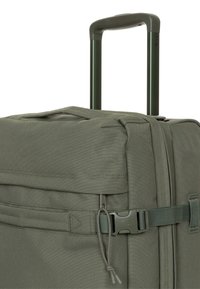 Bagaglio verde oliva con esterno in tessuto resistente, manico estensibile e chiusura con fibbia in plastica. Dotato di un ampio scomparto principale e di una cerniera.