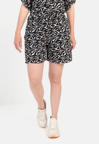 Sort og creme mønstrede shorts med elastisk talje, prydet med et blomsterdesign og sidelommer, parret med lette sneakers.