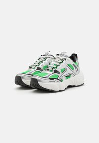 Chunky Sneaker mit einem Obermaterial aus weißem und schwarzem Stoff, grünen Mesh-Akzenten, strukturierter Sohle und Schnürdesign.