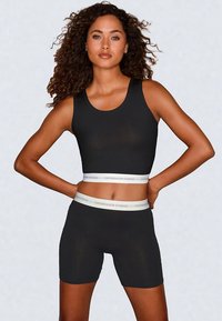Brassière de sport noire et short assorti présentent une légère brillance, une coupe ajustée et une bande élastique blanche avec logo à la taille.