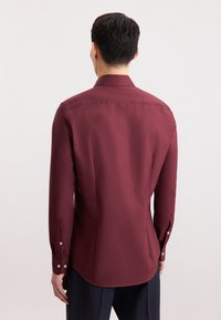 Camicia a maniche lunghe color mogano con colletto a punta, tessuto liscio, polsini abbottonati e orlo arrotondato, vista da dietro.