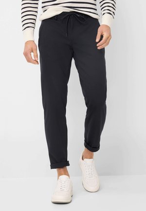 Marineblaue, leichte Hose mit elastischem Bund, schmaler Passform, geripptem Saum und Seitentaschen, getragen mit weißen Sportschuhen.