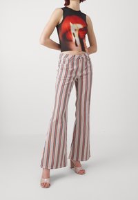 Personne portant un haut court sans manches avec un motif abstrait rouge et un pantalon évasé taille haute à rayures multicolores, accompagné de talons nus ouverts.