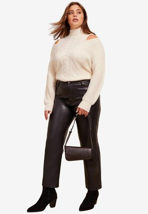 Maglione crema a trecce con design spalle scoperte, abbinato a pantaloni in pelle nera a vita alta e stivali con tacco neri alla caviglia.