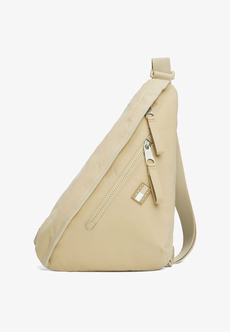 Borsa a tracolla beige con superficie testurizzata, dotata di una tasca frontale con zip e accento del logo. Cinghia regolabile e design angolato per un facile trasporto.