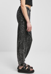 Svarte joggebukser med marmor mønster, elastisk midjebånd, innsnitt ved anklene og sidesømmer, kombinert med svarte flate sandaler.