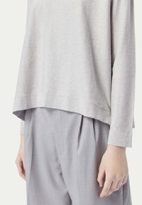 Ljusgrå långärmad topp med avslappnad passform och rundad nederkant, ihop med matchande ljusgrå plisserade byxor. Slät textur.