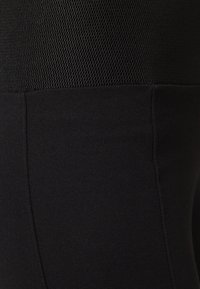 Zwarte sportleggings hebben een gemêleerd netpaneel aan de bovenkant en een gladde stof eronder. Het ontwerp benadrukt een getailleerde pasvorm.