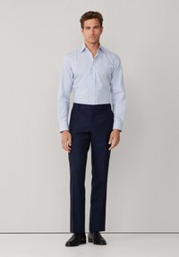 Chemise à rayures bleu clair et blanche à manches longues associée à un pantalon habillé navy et des chaussures noires. Design simple, silhouette ajustée, texture douce.