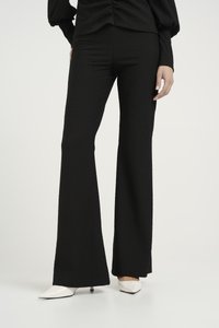 Svarte bukser med svampete stoff, med en glatt livlinje, stylet med spisse hvite hæler for en kontrasterende look.