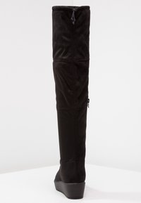 Svart knähög stövel gjord av mjukt mockaliknande material, med kilklack, sidodragkedja och justerbar dragsko upptill.