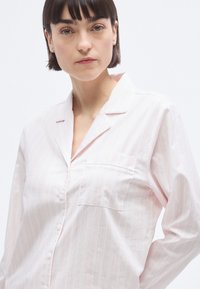 Chemise rayée rose clair à manches longues, avec boutons sur le devant et une poche poitrine unique. Le tissu semble doux avec une texture lisse.